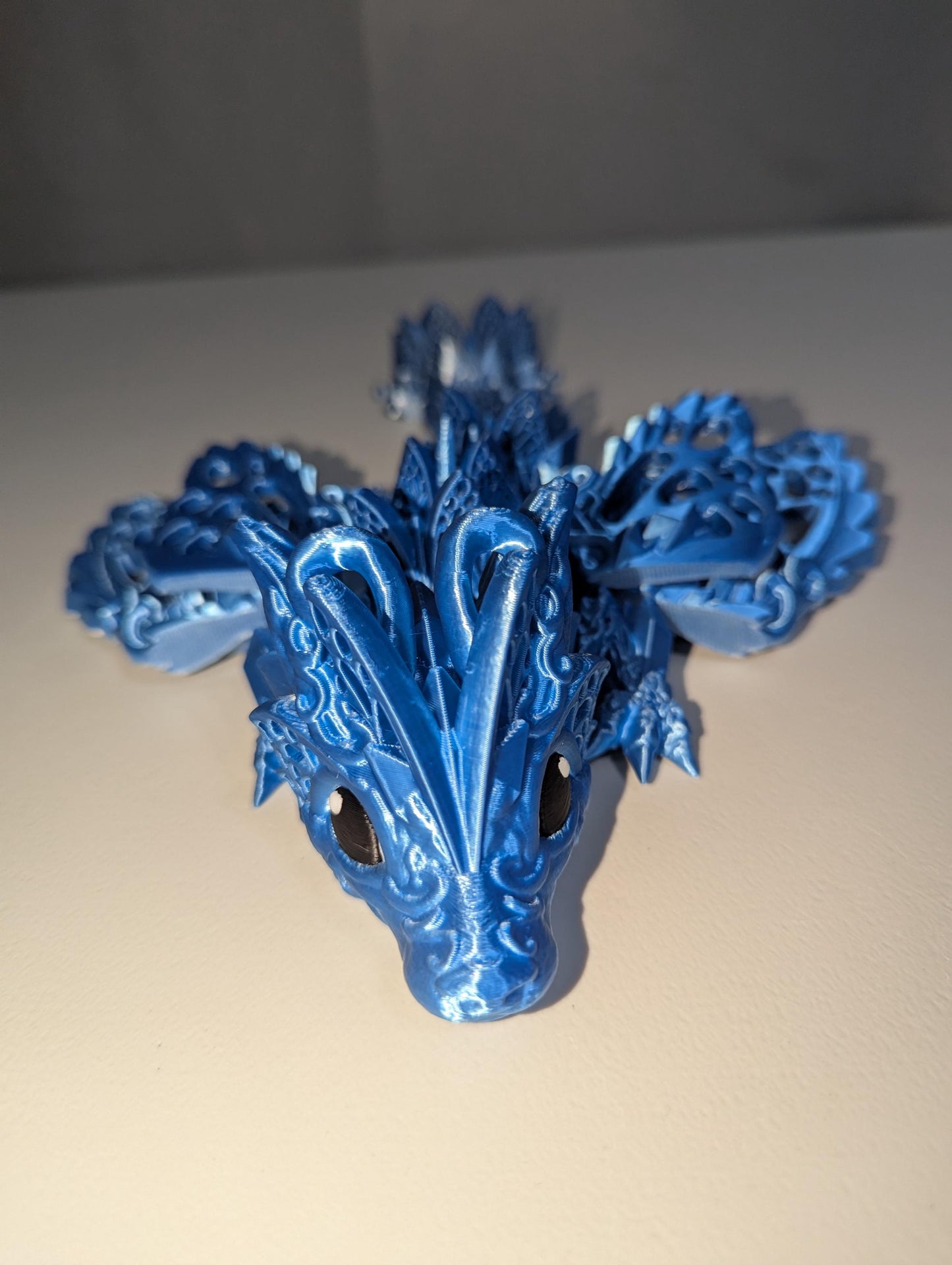 Forwarded facing up-close of face on the silver/blue winged baby articulated dragon.
