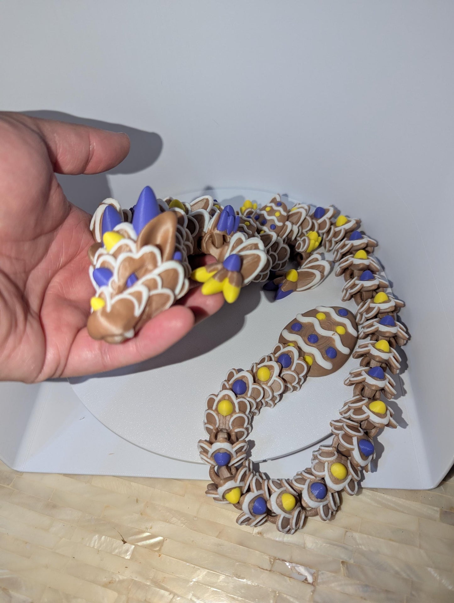 Articulated Easter Egg Dragon. Featuring four colors (Brown,white,yellow,and purple). Curled up with a large Easter egg tail. lifting head up in picture