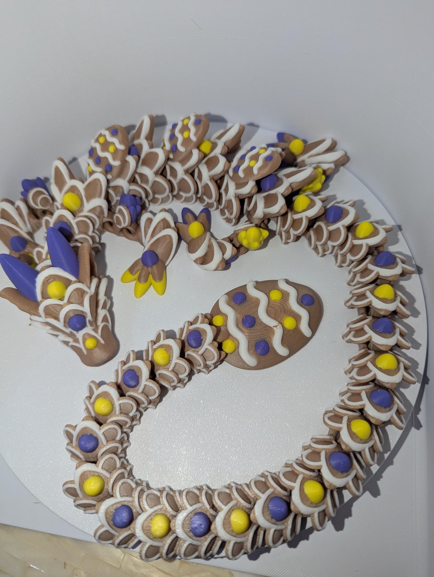 Articulated Easter Egg Dragon. Featuring four colors (Brown,white,yellow,and purple). Curled up with a large Easter egg tail.