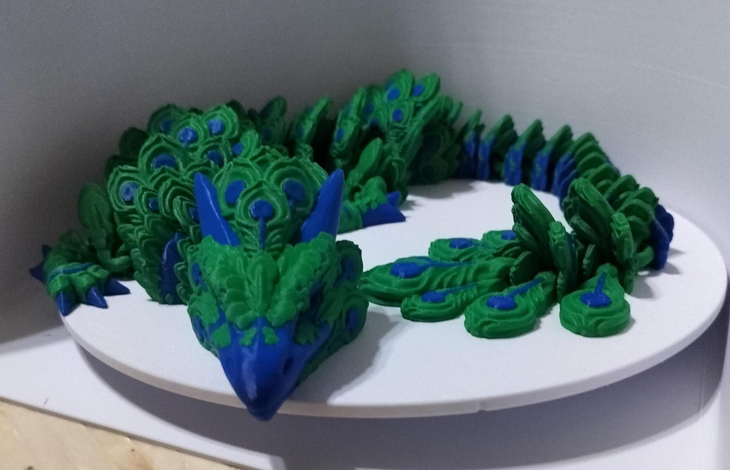 Peacock Articulated dragon featuring a rich green and blue color scheme.with out stretched feathered tail. front profile